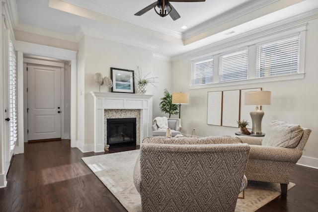 living room with a tray ceiling, ceiling fan, dark wood-type flooring, a glass covered fireplace, and crown molding