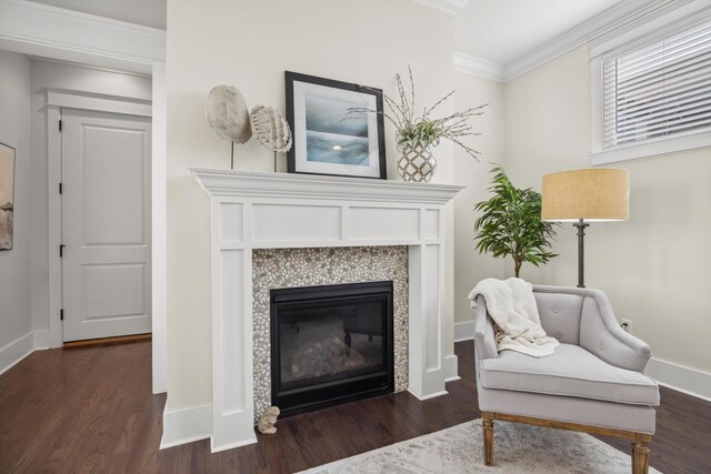 living area featuring baseboards, wood finished floors, a tiled fireplace, and crown molding