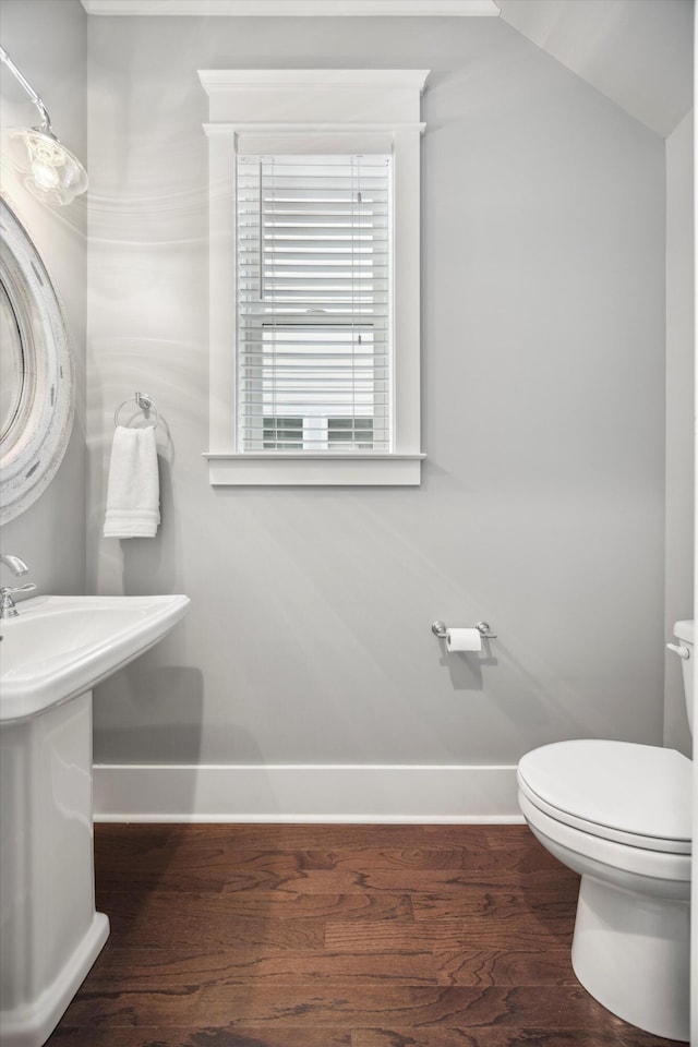 half bath featuring a sink, baseboards, toilet, and wood finished floors