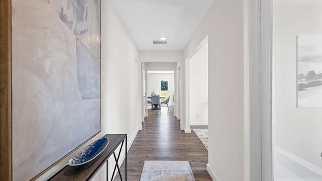 hall featuring visible vents, baseboards, and dark wood-style flooring