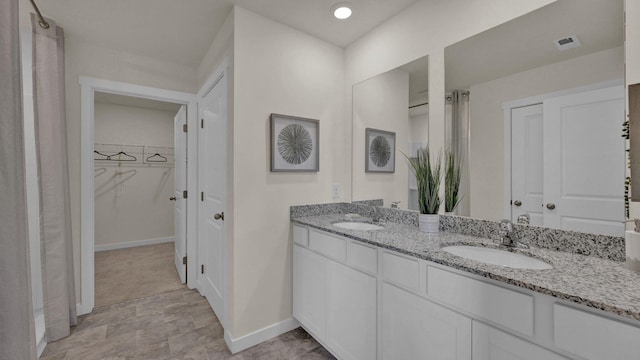 bathroom featuring double vanity, a spacious closet, baseboards, and a sink