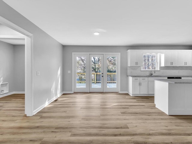 kitchen with tasteful backsplash, light wood-style flooring, baseboards, a sink, and white cabinets