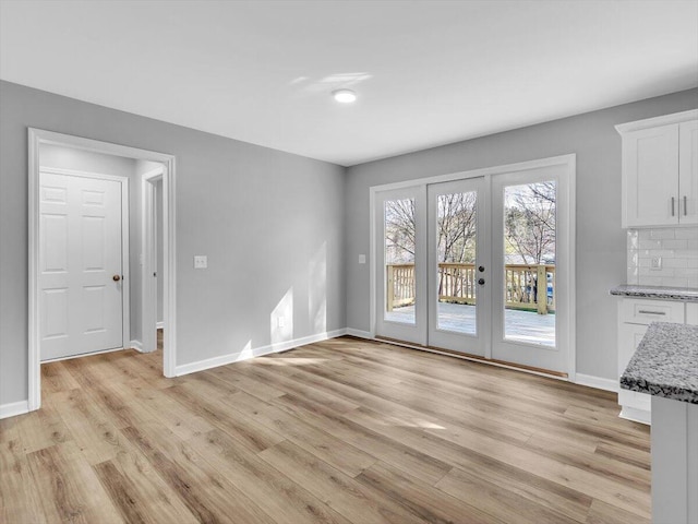 unfurnished living room featuring french doors, baseboards, and light wood-style floors