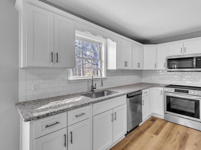 kitchen featuring tasteful backsplash, light wood-type flooring, stainless steel appliances, a sink, and white cabinets