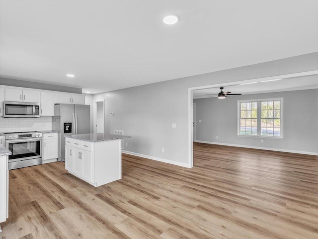 kitchen with a ceiling fan, a kitchen island, appliances with stainless steel finishes, open floor plan, and white cabinets