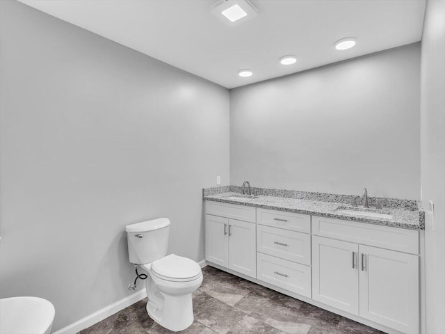 bathroom with toilet, a sink, double vanity, and baseboards