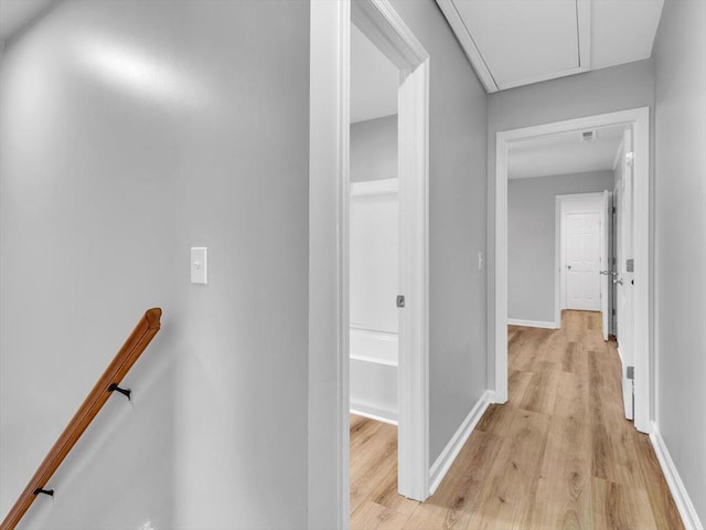 corridor featuring attic access, an upstairs landing, baseboards, and light wood-style floors