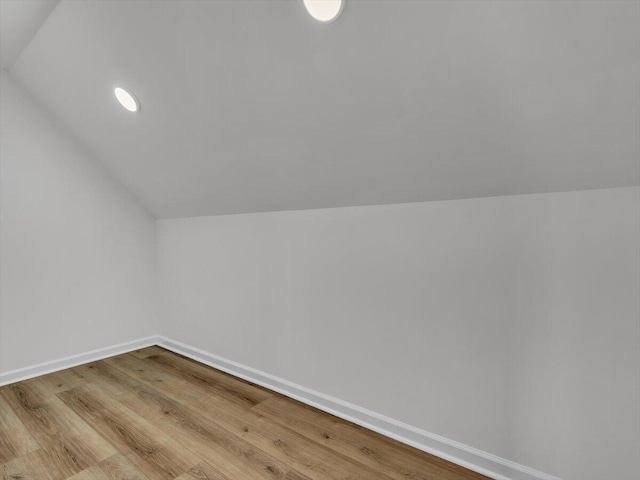 additional living space with baseboards, wood finished floors, and vaulted ceiling