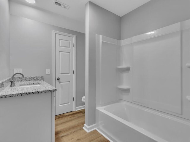 bathroom with toilet, vanity, wood finished floors, baseboards, and visible vents