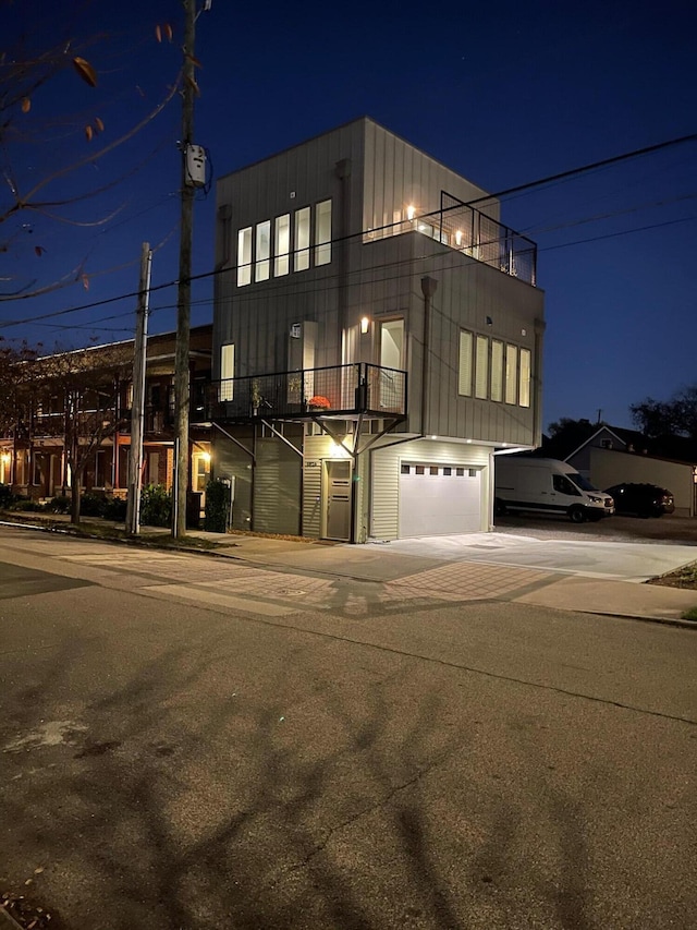295 W 19th St, Chattanooga, TN 37408 - property exterior at night featuring a balcony, an attached garage, board and batten siding, and concrete driveway