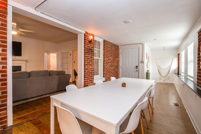 dining room featuring a fireplace, brick wall, baseboards, visible vents, and dark wood-type flooring
