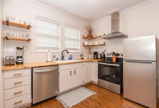 kitchen featuring ornamental molding, wall chimney exhaust hood, appliances with stainless steel finishes, a sink, and open shelves