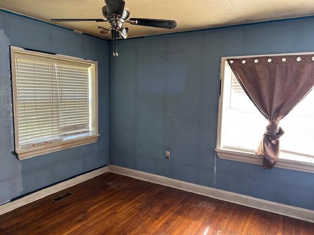 empty room with wood finished floors, a ceiling fan, visible vents, and baseboards