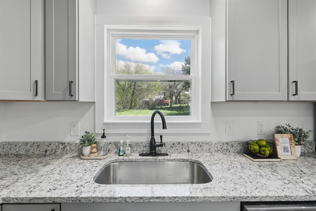 kitchen featuring dishwasher, a sink, and light stone countertops