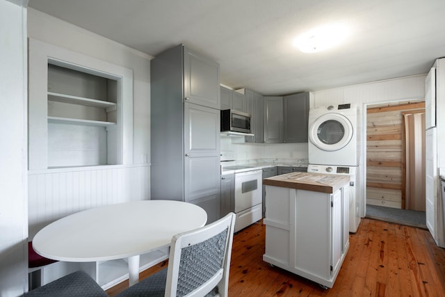 kitchen featuring white electric stove, light wood finished floors, stacked washing maching and dryer, butcher block counters, and stainless steel microwave