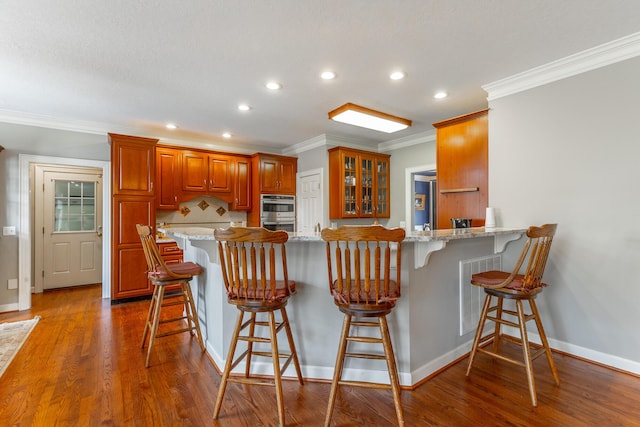 kitchen featuring crown molding, a kitchen breakfast bar, a peninsula, visible vents, and recessed lighting