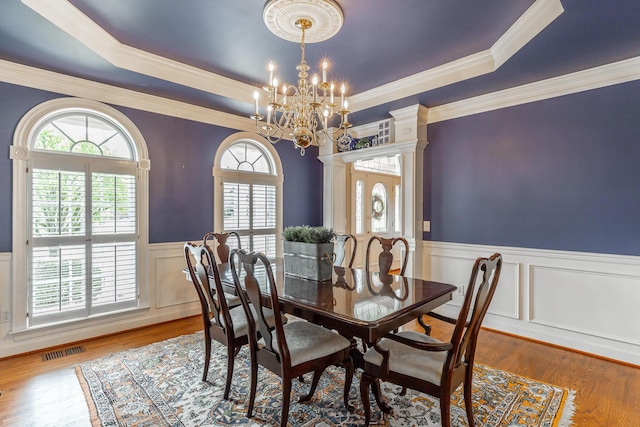 dining room featuring a wainscoted wall, a tray ceiling, visible vents, a chandelier, and wood finished floors