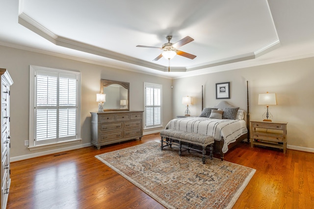 bedroom featuring baseboards, ornamental molding, wood finished floors, and a tray ceiling