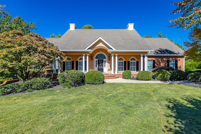 view of front of house featuring a front yard, roof with shingles, a chimney, and covered porch