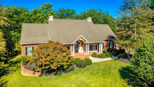 view of front of property featuring a front lawn, brick siding, a chimney, and roof with shingles