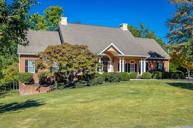 view of front of property featuring a chimney, brick siding, a shingled roof, and a front yard