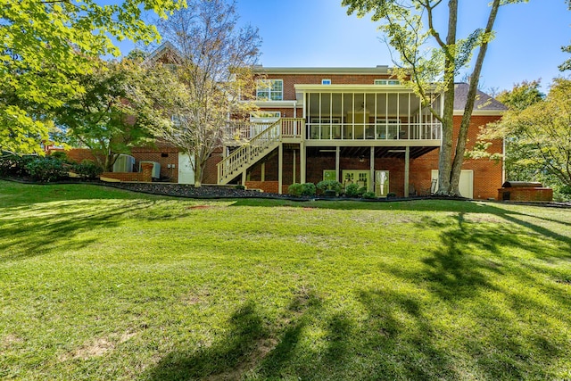 rear view of property featuring brick siding, a sunroom, a yard, and stairs