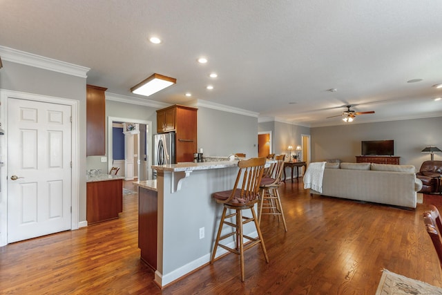 kitchen with a ceiling fan, freestanding refrigerator, crown molding, open floor plan, and a breakfast bar area