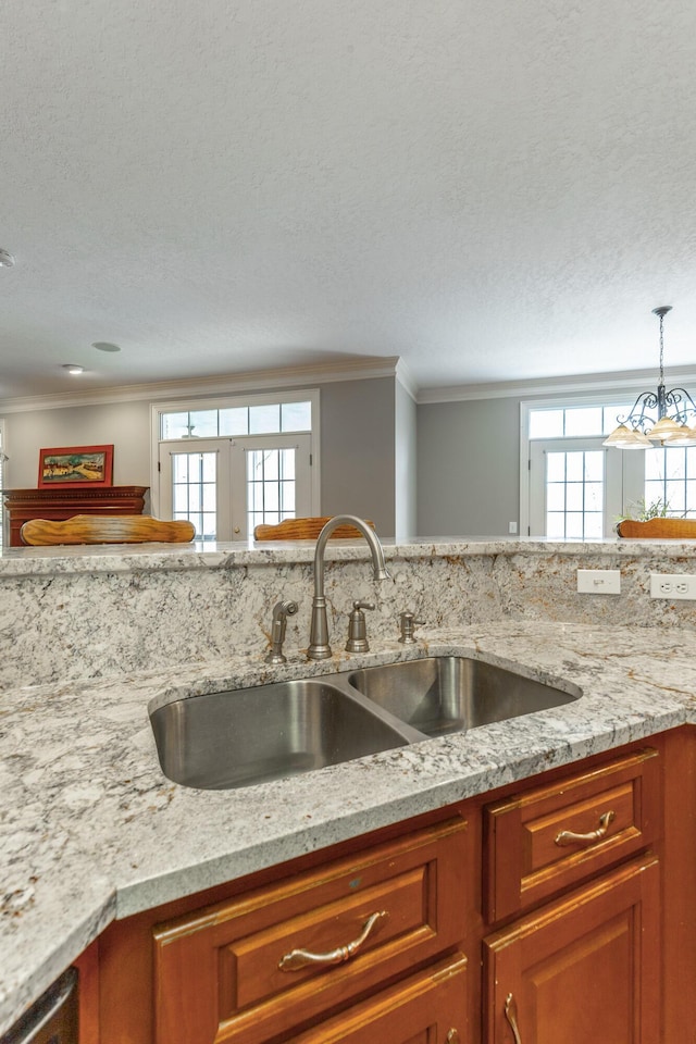 kitchen featuring brown cabinets, a sink, crown molding, pendant lighting, and a textured ceiling