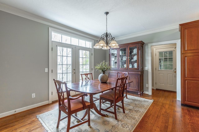 dining area with baseboards, crown molding, french doors, and a chandelier
