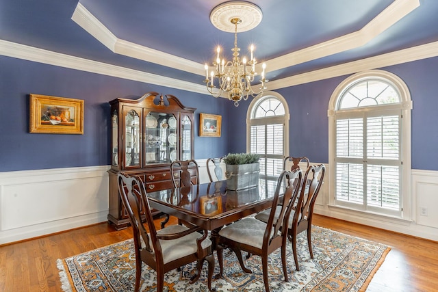 dining area featuring a wainscoted wall, a tray ceiling, an inviting chandelier, wood finished floors, and crown molding