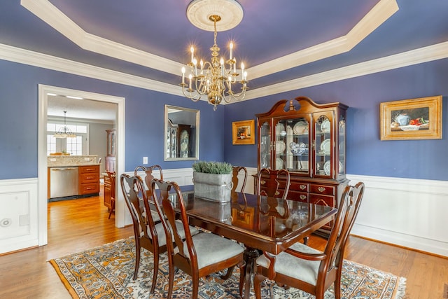 dining space featuring a wainscoted wall, ornamental molding, a notable chandelier, and a raised ceiling