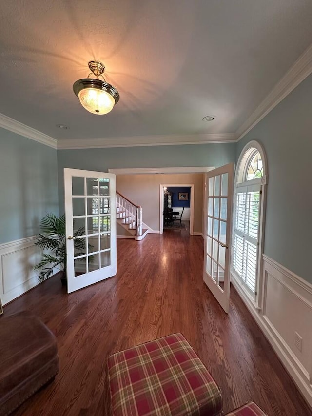 unfurnished living room with wood finished floors, wainscoting, ornamental molding, and french doors
