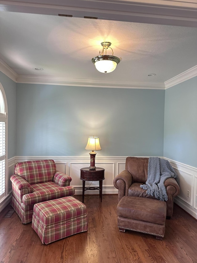 living area with a decorative wall, crown molding, a wainscoted wall, and wood finished floors