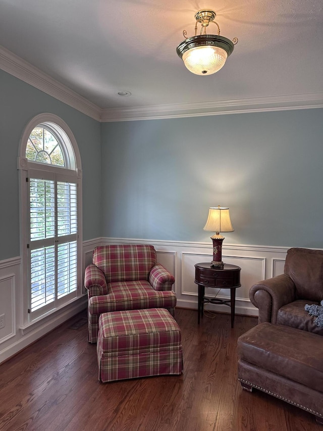 living area featuring a decorative wall, dark wood-style flooring, a wainscoted wall, and crown molding