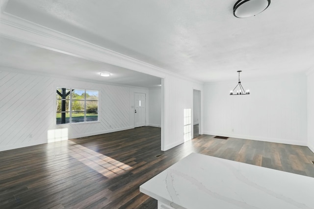 unfurnished living room with dark wood-style floors, a chandelier, and ornamental molding