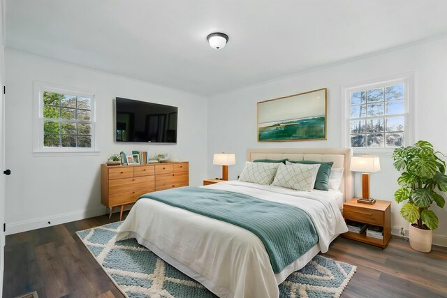 bedroom featuring baseboards, crown molding, wood finished floors, and multiple windows