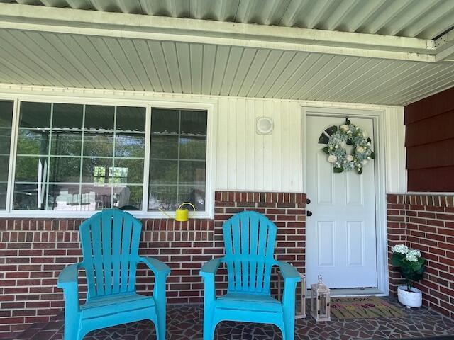 doorway to property with a porch and brick siding