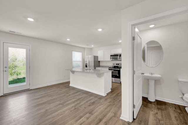 kitchen with white cabinets, a kitchen island with sink, appliances with stainless steel finishes, and wood finished floors