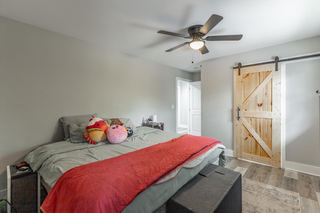 bedroom with wood finished floors, ceiling fan, baseboards, and a barn door