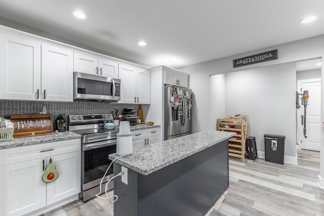 kitchen featuring light wood-style flooring, backsplash, white cabinets, light stone countertops, and appliances with stainless steel finishes