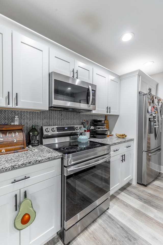 kitchen featuring light wood-style flooring, white cabinets, appliances with stainless steel finishes, and decorative backsplash