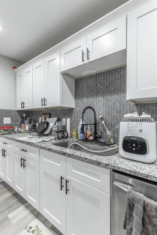 kitchen featuring light wood-type flooring, white cabinetry, a sink, and backsplash