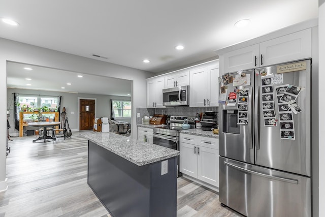 kitchen featuring visible vents, a center island, light stone counters, stainless steel appliances, and decorative backsplash