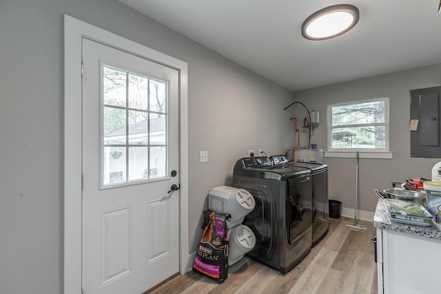 clothes washing area featuring light wood finished floors, washing machine and clothes dryer, cabinet space, and electric panel