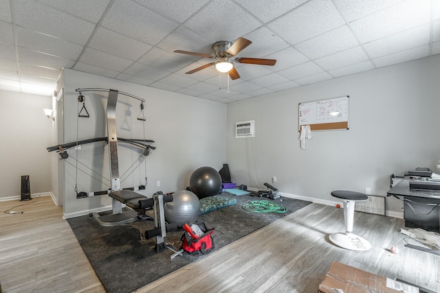 exercise room with an AC wall unit, baseboards, a ceiling fan, and wood finished floors