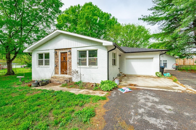 single story home with an attached garage, aphalt driveway, a front lawn, and brick siding