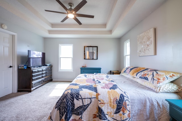 carpeted bedroom with ceiling fan and a raised ceiling