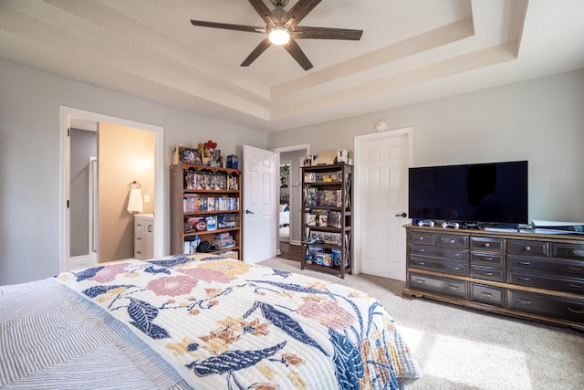 bedroom with ensuite bathroom, a tray ceiling, ceiling fan, and light carpet