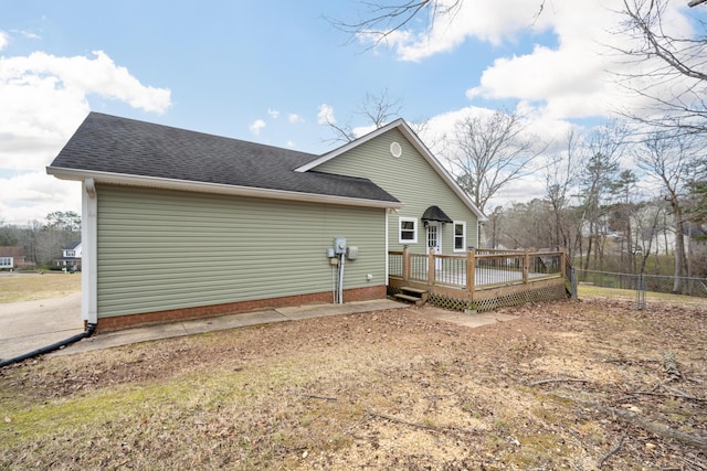 rear view of property with fence, a shingled roof, and a deck