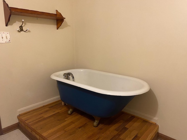 full bath with baseboards, a soaking tub, and wood finished floors